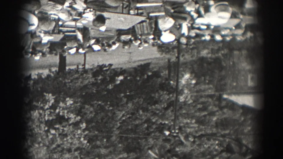 1938 New Jersey home-movie view across trees and lamp posts toward an outdoor gathering space with people in the distance.