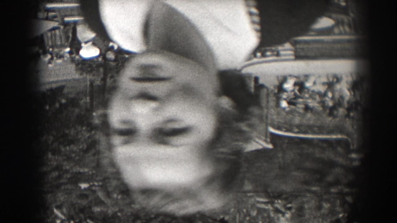 A blurred upside-down view shows a woman near a garden path in 1938 New Jersey, with foliage and a large building in the background.