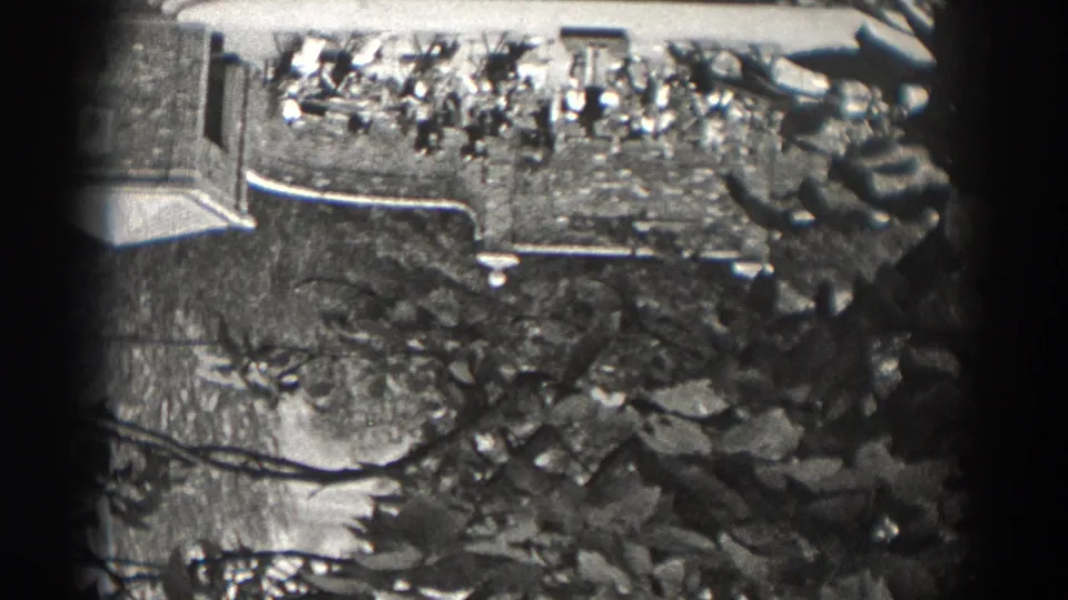 The garden remains in view with two women partly visible near plants, stone edging, and the side of a large building in 1938 New Jersey.