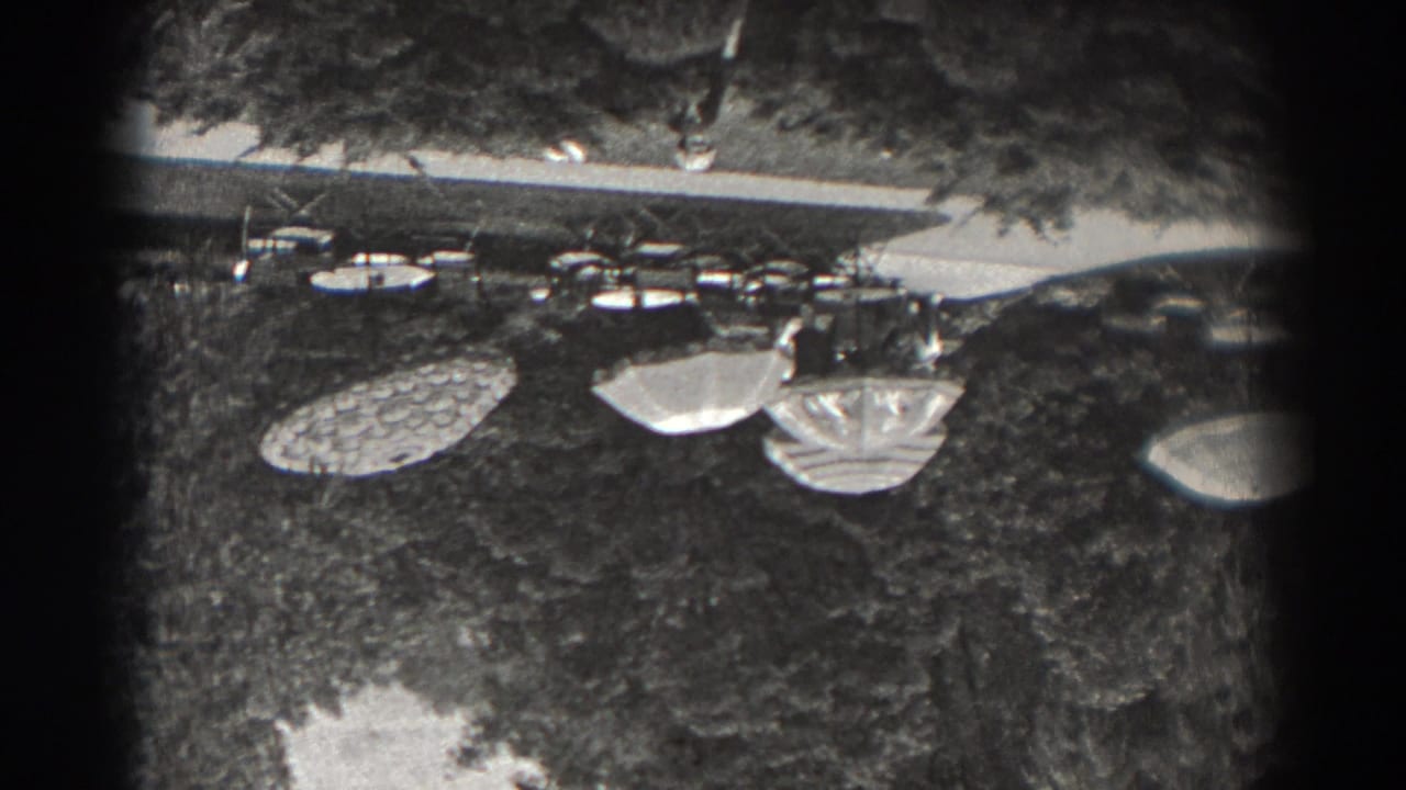 1938 New Jersey 8mm frame showing garden tables and patterned umbrellas on grass beneath trees.