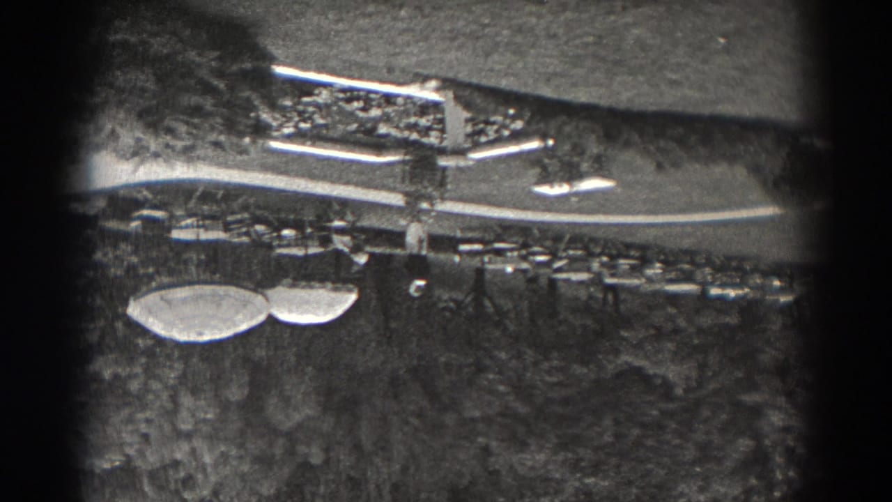 1938 New Jersey 8mm frame showing an upside-down elevated view of lawns, trees, curving paths, and a long low park structure.