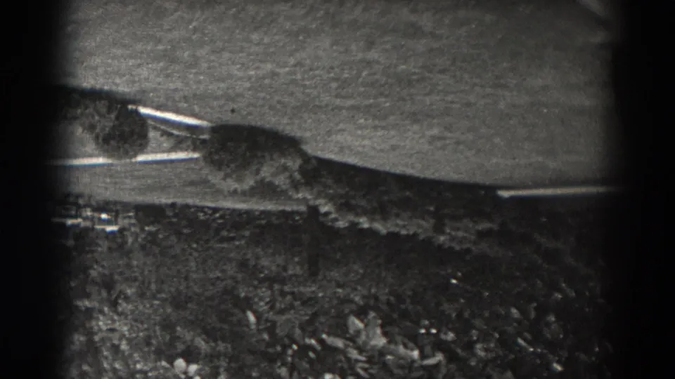 Upside-down 1938 New Jersey home-movie frame showing a paved surface, rough grass, and low plants with dark 8mm frame edges.