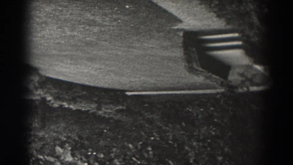 Inverted 1938 home-movie frame showing pavement, lawn, and a small hard-edged feature, with strong black side vignetting.