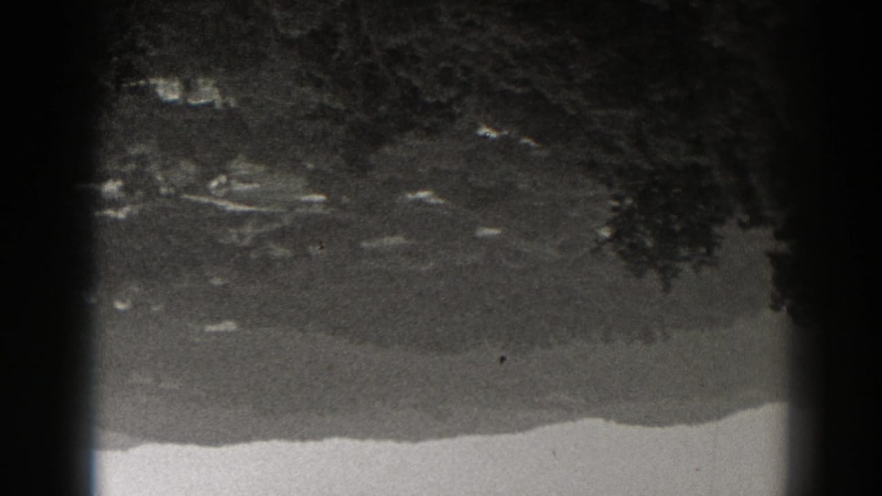 Inverted 1938 New Jersey 8mm view of scattered buildings and trees at the base of a rugged slope.