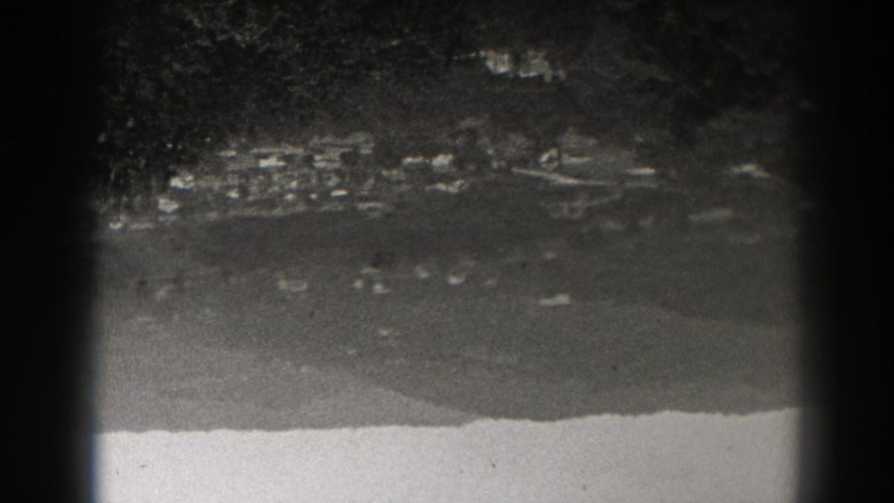 Dark grainy landscape with faint distant lights and a pale foreground band.
