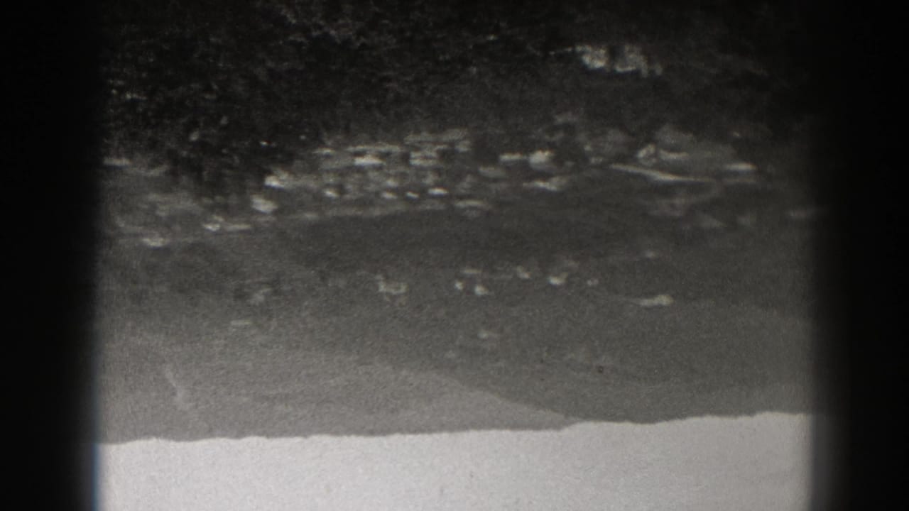 Dim distant terrain or shoreline with scattered small lights under dark shapes.