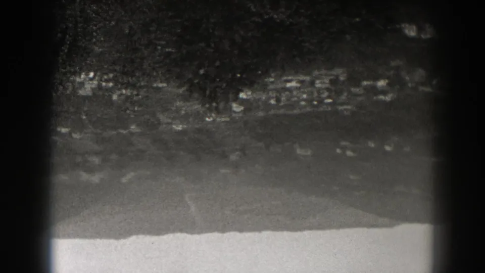 Upside-down 1938 New Jersey 8mm frame showing a distant town, wooded hillside, pale road lines, and dark gate edges.