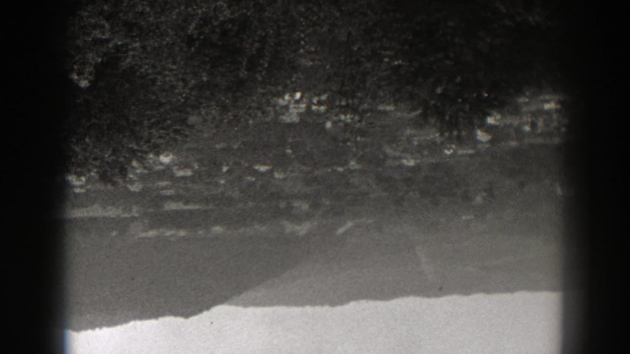 1938 New Jersey 8mm frame showing rippled lake water reflecting trees and a distant slope, with dark gate edges visible.