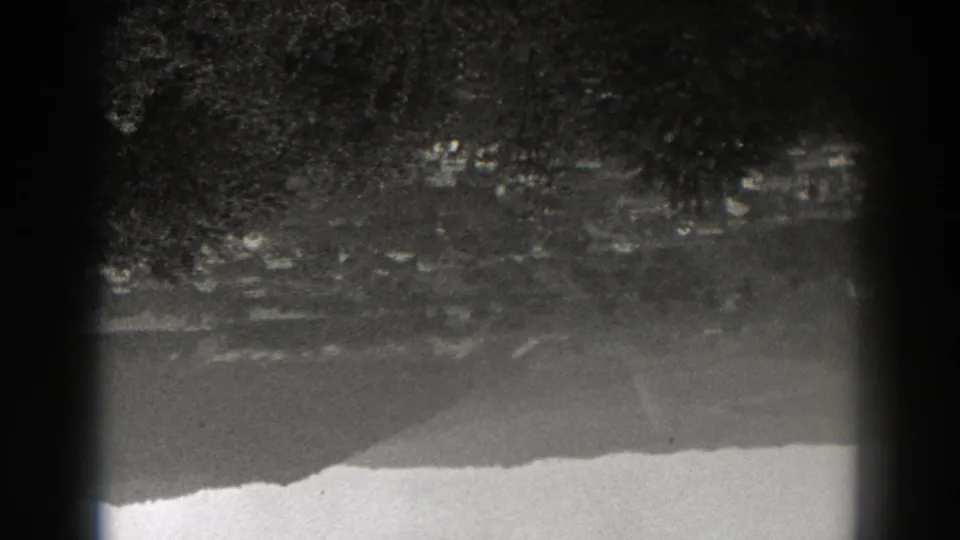 1938 New Jersey 8mm frame showing rippled lake water reflecting trees and a distant slope, with dark gate edges visible.