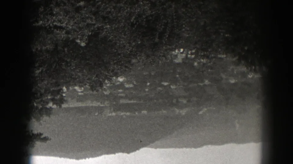 1938 New Jersey 8mm still showing dark reflected trees, muted lake water, and a bright shoreline edge in black and white.