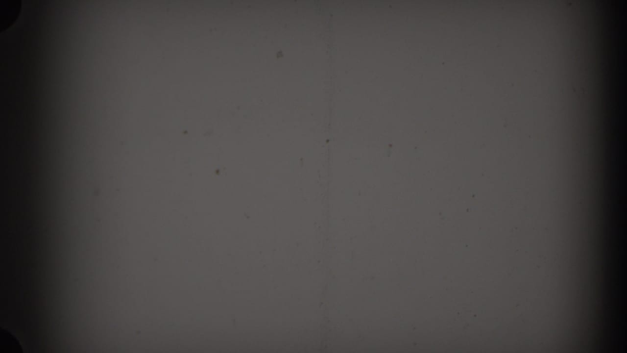 Dark monochrome film frame with dust, scratches, and a vertical shadow band.