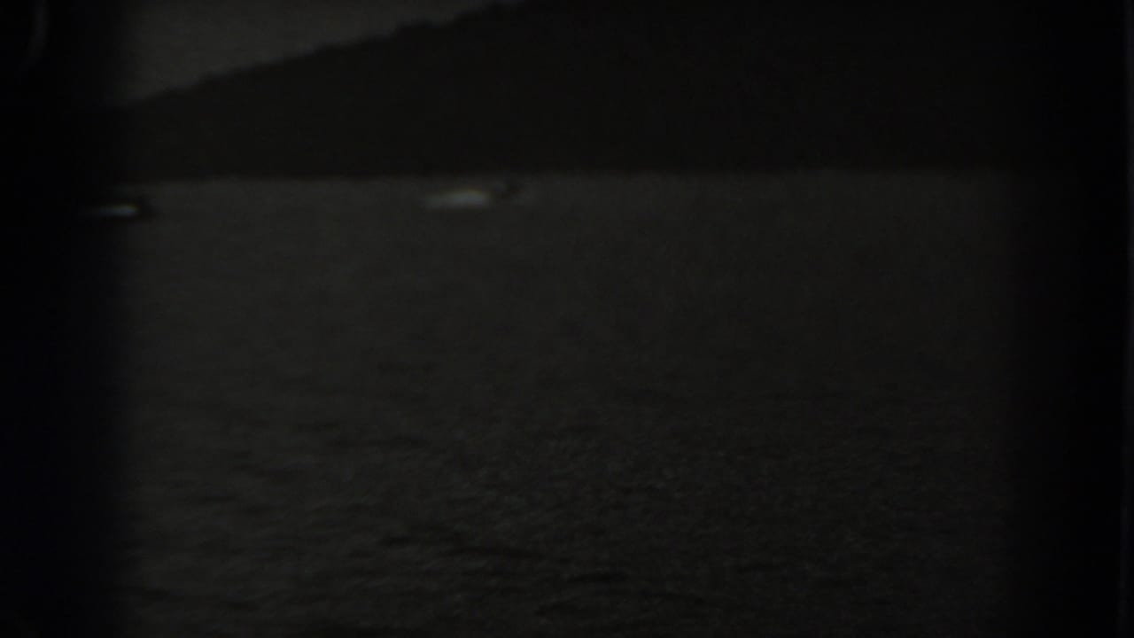 Dark water with a faint shoreline silhouette and small pale shape near the horizon.
