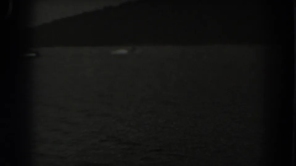 1938 New Jersey 8mm frame showing very dark water, a distant shore silhouette, and a barely visible pale object near the horizon.