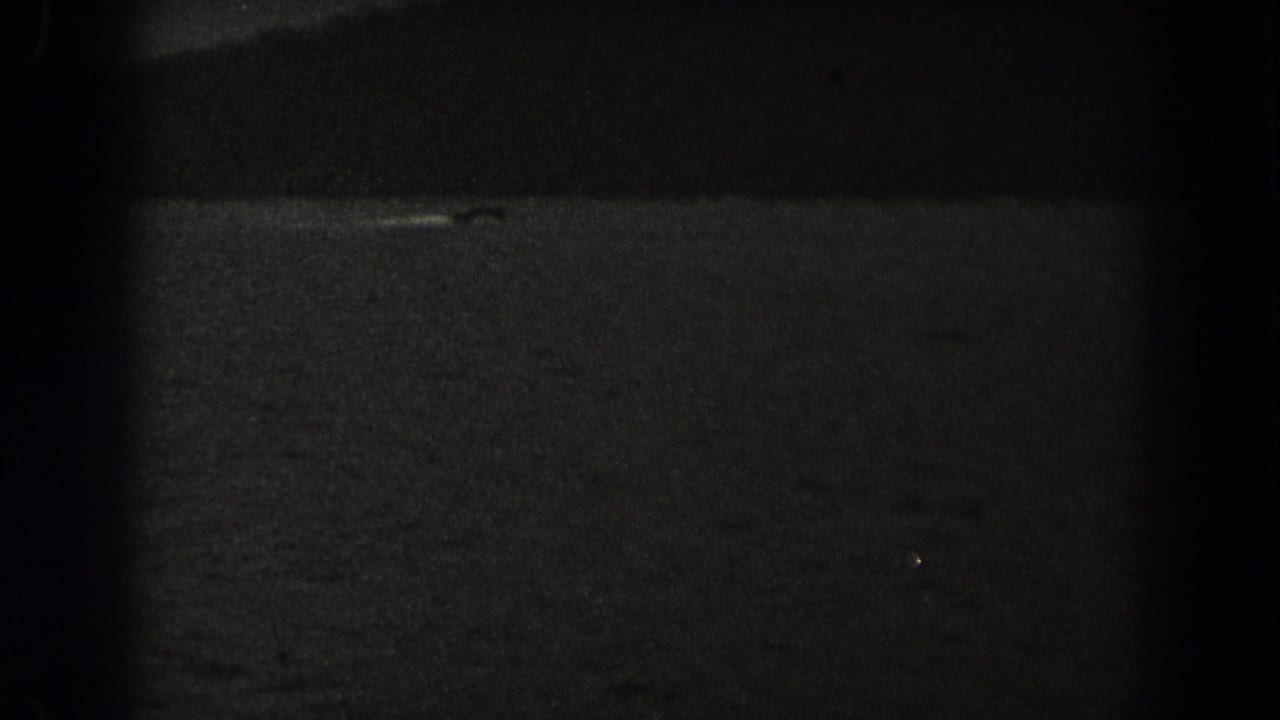 Low-light 1938 New Jersey frame with dark water, a faint pale streak, and a small dark shape that may be a boat.