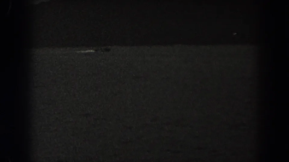 Underexposed 8mm frame from New Jersey showing rippled water and a faint light-toned mark with little visible detail.