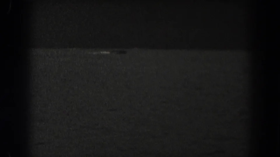 Final 1938 New Jersey frame showing dark, grainy water and a small pale streak near the distant shoreline area.