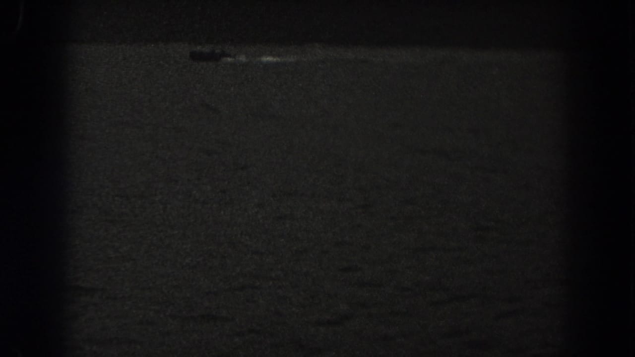 Small boat crossing dark lake water with a faint wake near the top of frame.