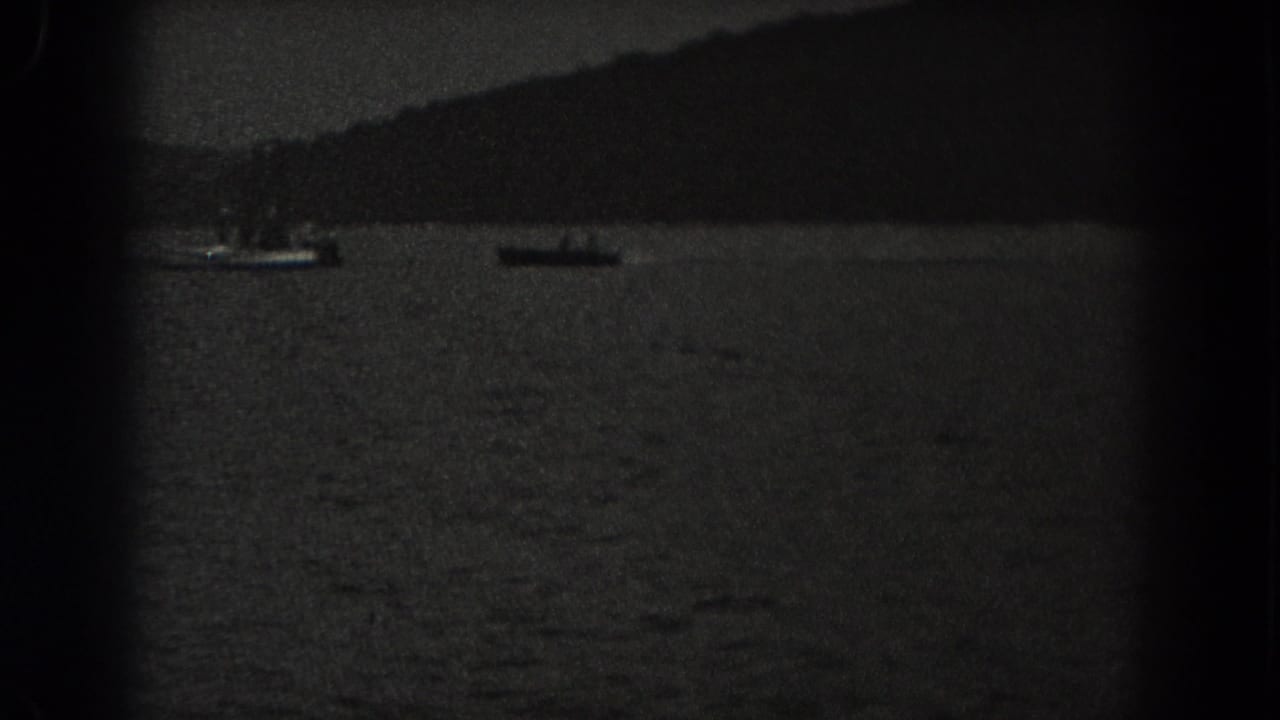 Two small boats on a dark lake with a wooded shoreline in the distance.