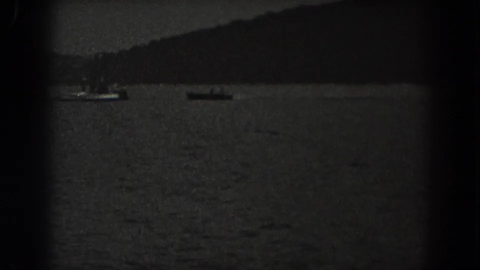 1938 New Jersey 8mm frame showing small boats on a dim lake, with tree-covered hills beyond the water.