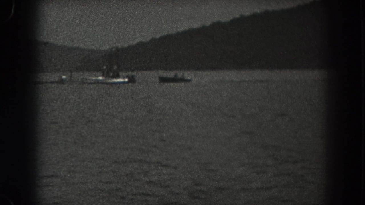 1938 New Jersey home-movie frame with two small boats on lake water and a tree-lined hillside in the background.