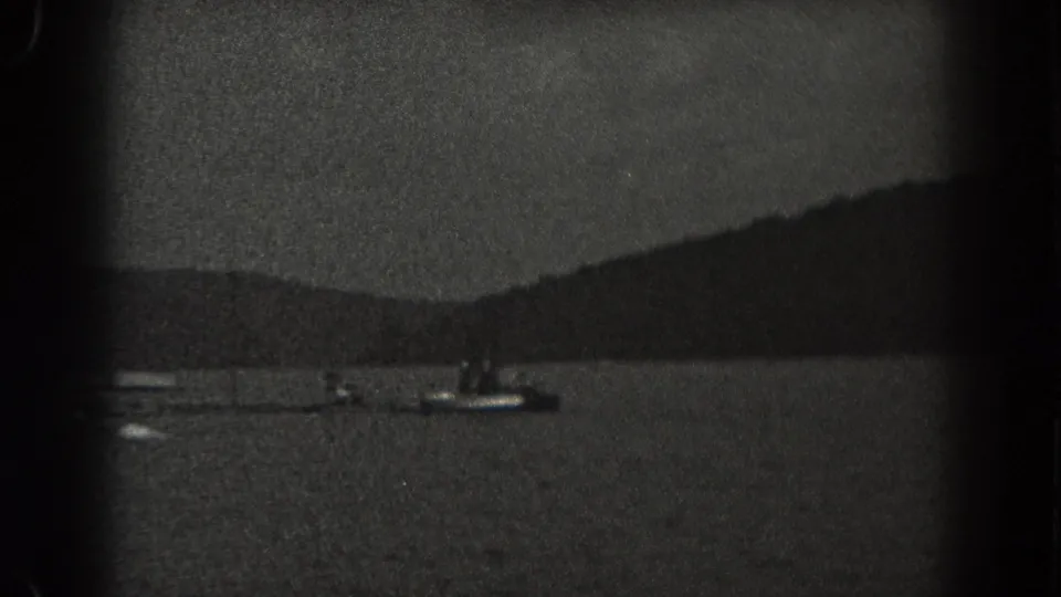 Grainy 1938 New Jersey 8mm frame of small boats on a lake, with distant people or figures indistinct on the craft.