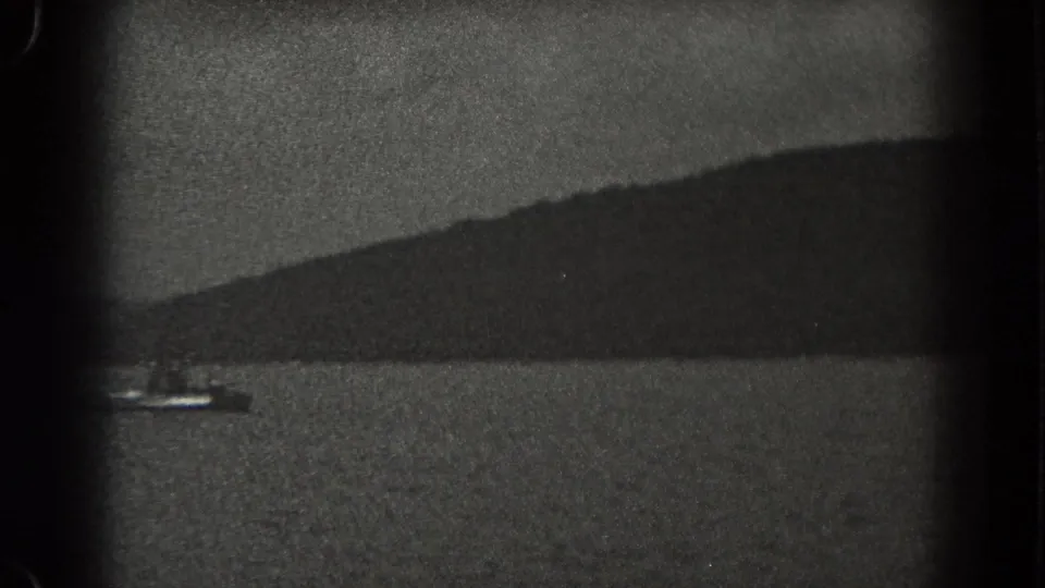 1938 New Jersey lake footage frame with a small boat partly near the edge, open water, and dark wooded hills beyond.
