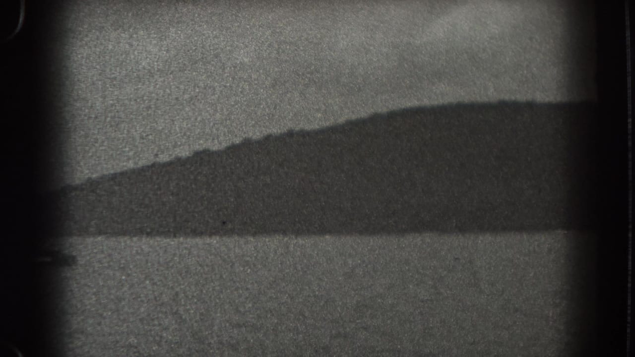 Grainy black-and-white lake surface with a dark shoreline and film gate edges.