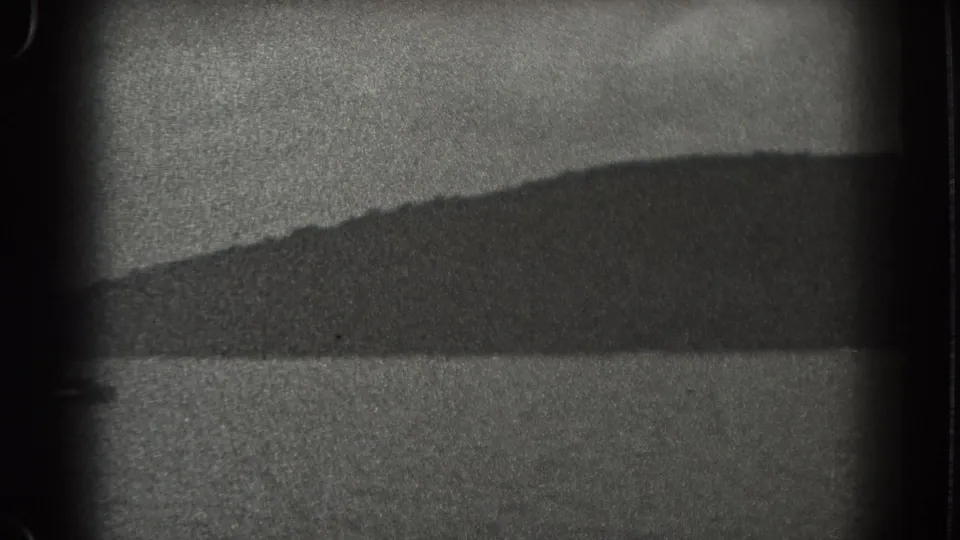 1938 New Jersey 8mm frame showing rippled lake water from a boat, with a dark shoreline and low land in the distance.