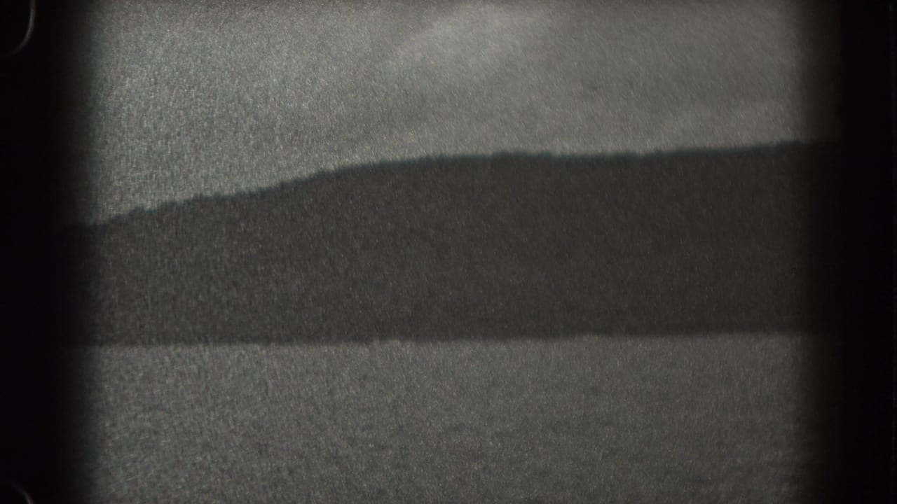 1938 New Jersey lake view from a boat, with shadowed shoreline, low wooded land, and visible 8mm gate edges.