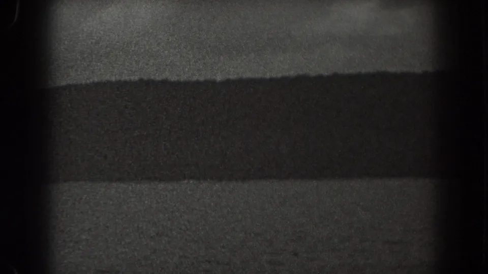 1938 New Jersey 8mm footage frame with rippled water in front and a dark, low shoreline stretching across the background.