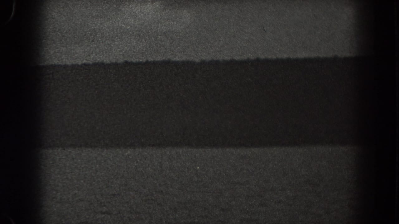 Dark water and hillside silhouette under a dim sky in grainy black-and-white film.