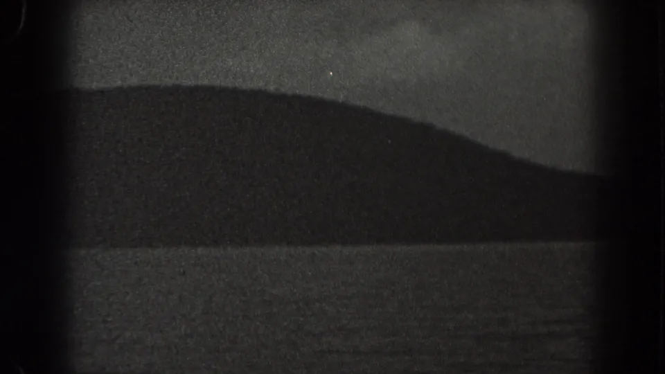 1938 New Jersey coastal home-movie frame showing a rounded dark ridge over calm water in grainy night exposure.