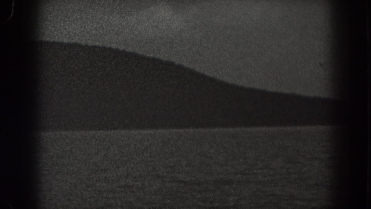 Distant dark ridge above rippled water under a pale sky.
