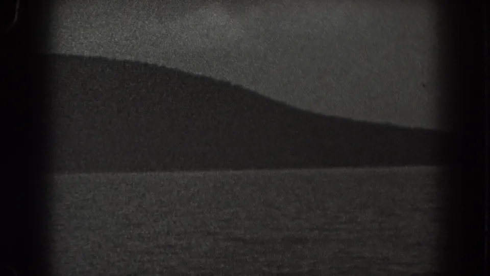 1938 New Jersey 8mm frame showing rippled water in the foreground and a dark distant ridge under a pale sky.