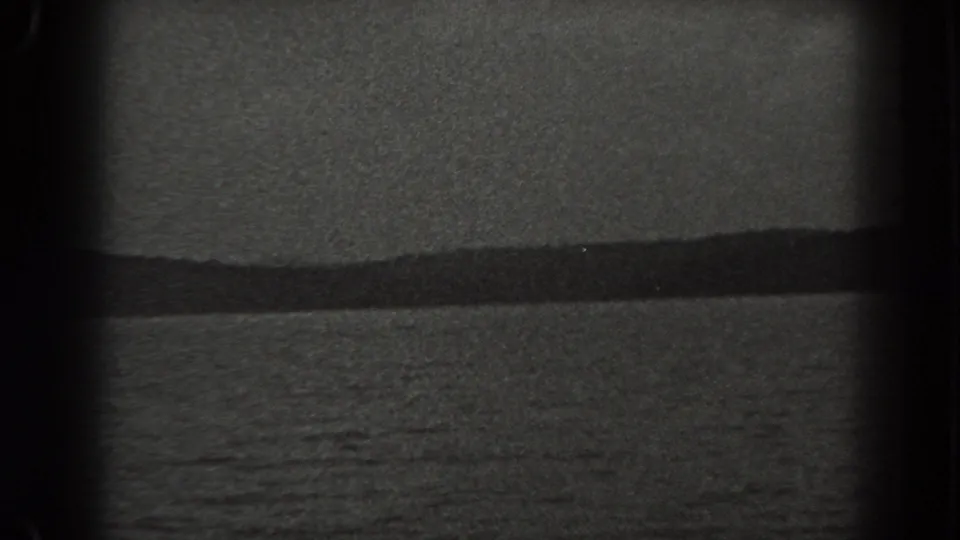 1938 New Jersey shoreline view on 8mm film, with rippling water, a dark horizon ridge, and heavy grain.