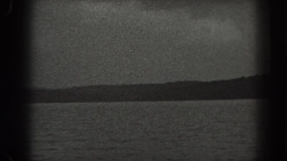 1938 New Jersey 8mm frame showing calm water, a low forested hill, muted sky, and dark film-edge vignetting.
