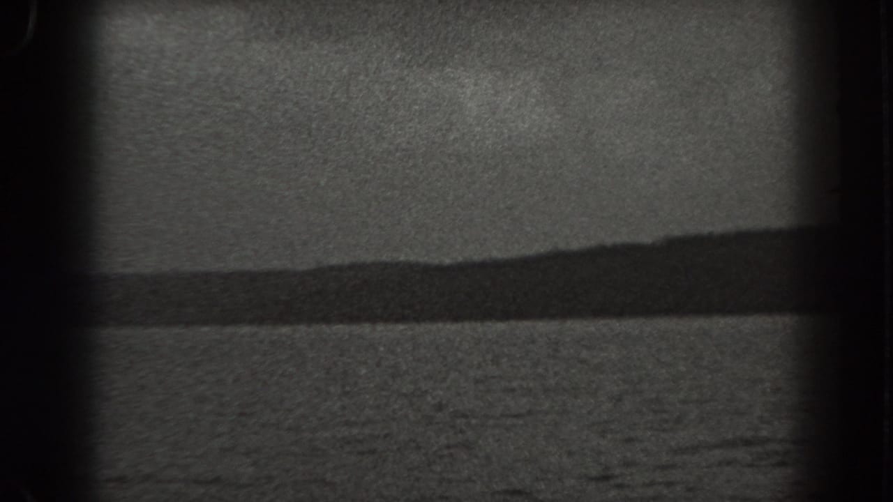 1938 New Jersey 8mm frame with rippled water in the foreground and a dark, undulating wooded shoreline beyond.