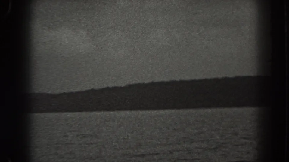 1938 New Jersey home-movie frame showing a grainy waterscape, dark tree-lined hill, pale sky, and visible film border shadow.