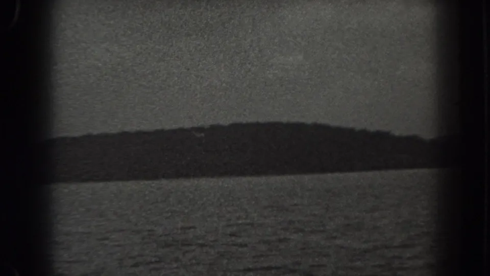 1938 New Jersey 8mm frame showing water, a distant wooded hill, muted sky, and pronounced dark vignetting at the frame edges.
