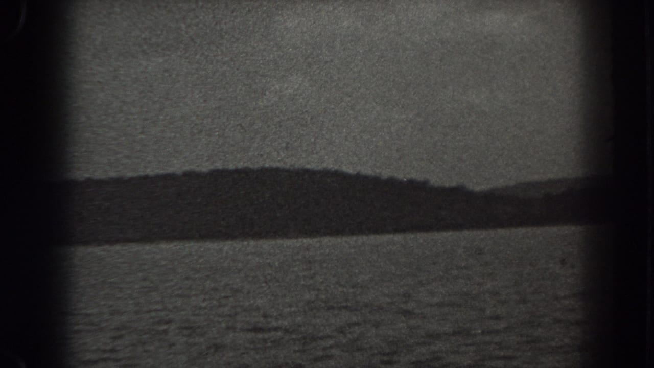 1938 New Jersey 8mm frame showing a broad lake, distant tree-lined shore, low hills, and overcast sky.