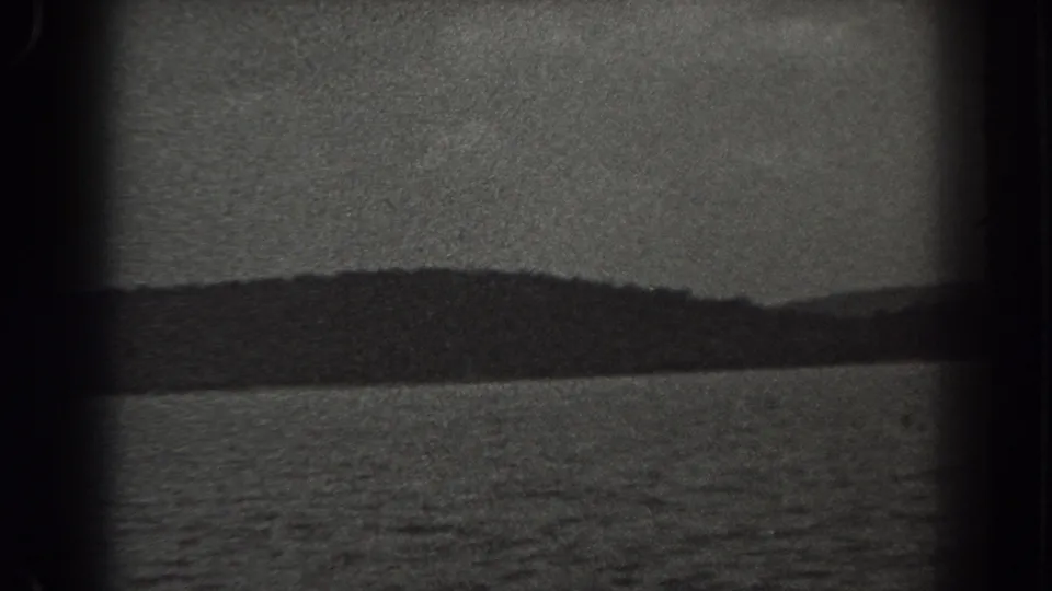 1938 New Jersey 8mm frame showing a broad lake, distant tree-lined shore, low hills, and overcast sky.