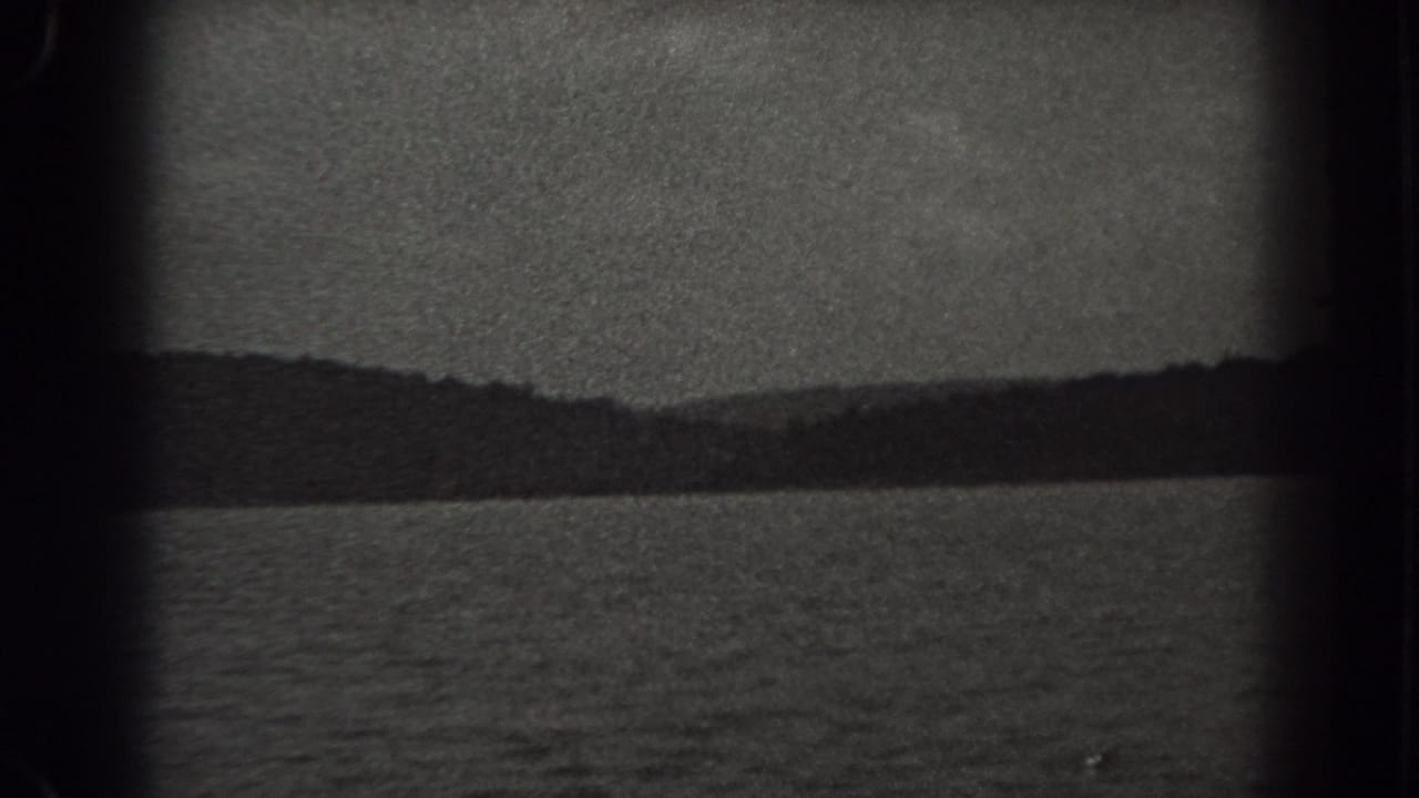 1938 New Jersey lake scene with rippled water in the foreground and a dark wooded shore beneath cloud cover.