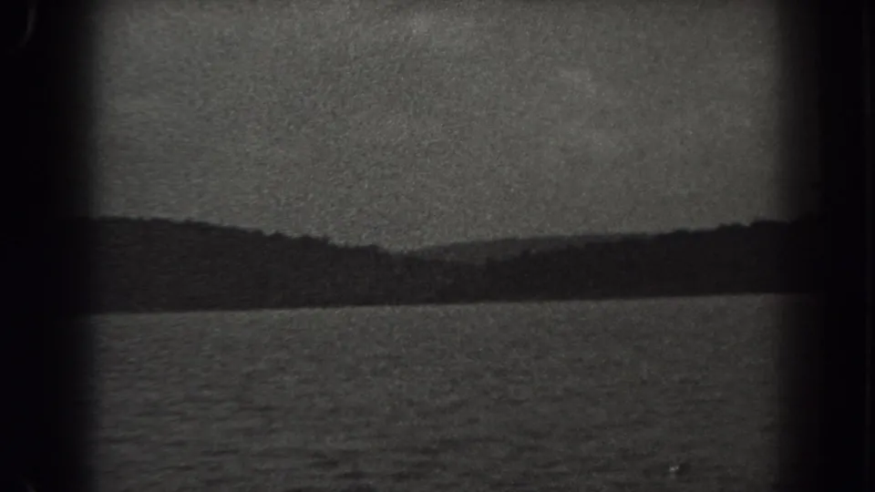 1938 New Jersey lake scene with rippled water in the foreground and a dark wooded shore beneath cloud cover.
