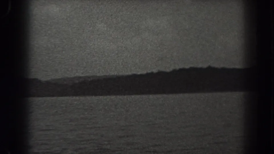 Black-and-white 8mm view of a New Jersey lake, with water, distant trees, and cloudy sky visible through frame edges.