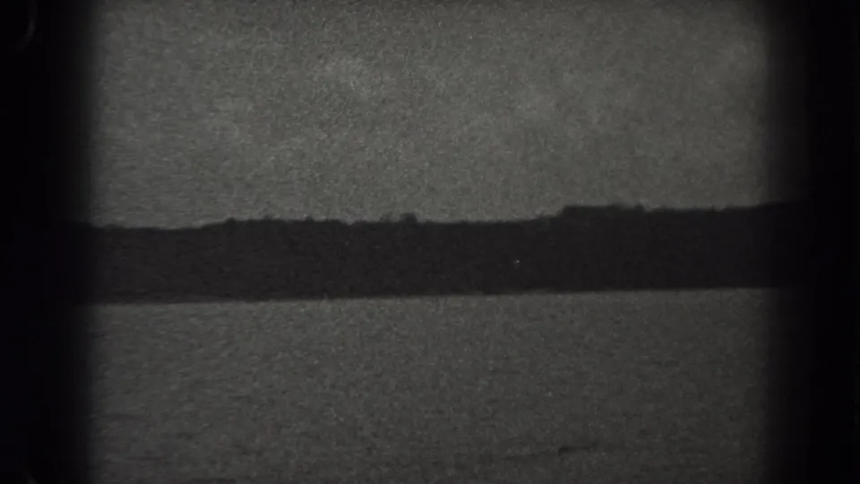 1938 New Jersey home-movie frame with a distant dark shoreline, gray sky, soft focus, grain, and visible gate shadows around the edges.