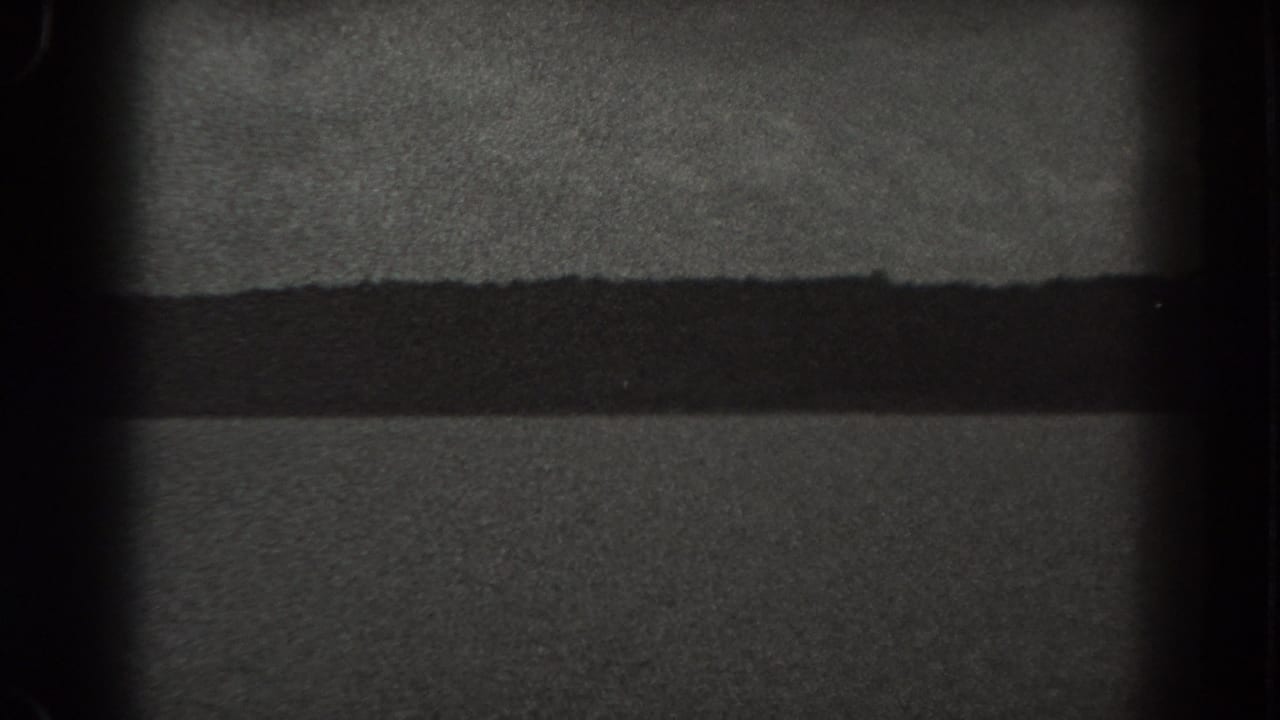 Grainy black and white water and distant shoreline framed by dark film edges.