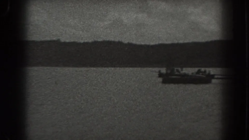 1938 New Jersey waterfront frame showing a small boat near a dock, distant shore, and tiny indistinct people aboard or nearby.