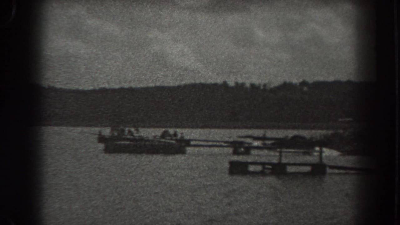 Small boats and a low dock or float on a lake with a wooded shoreline beyond.