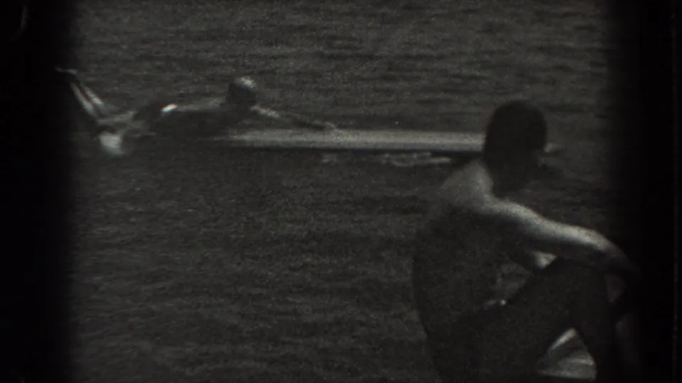 1938 New Jersey lake scene with a seated man in dark shorts in the foreground and a person stretched on a long board behind him.
