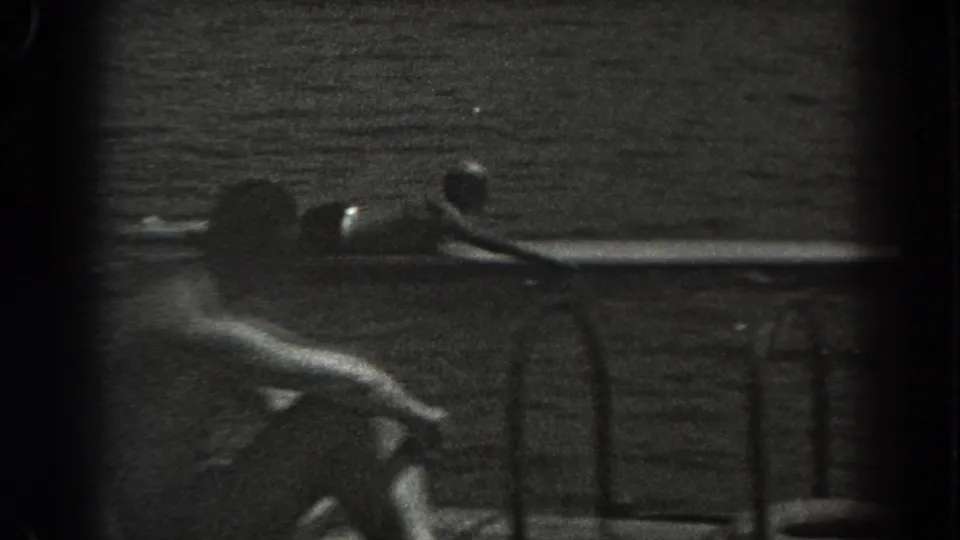 1938 New Jersey 8mm frame with a seated man near the foreground and another person lying on a board beside a lake dock or float.